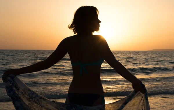 Silhouet van de vrouw permanent tegen zonsondergang met pareo. — Stockfoto