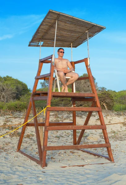 Uomo seduto sulla torre del bagnino sulla spiaggia . — Foto Stock