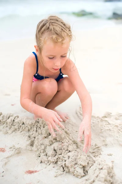 Kleines Mädchen spielt mit Sand am Strand. — Stockfoto