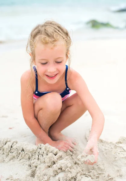 Маленькая улыбающаяся девочка играет с песком на пляже . — стоковое фото
