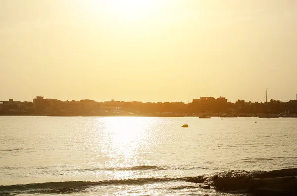 Sunset over the sea and city. Photograph from the beach. — Stock Photo, Image