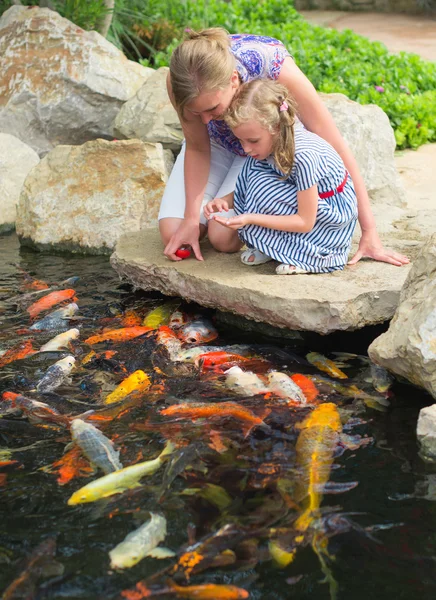 Woman and daughter feeding fishes in pond. — Stock Photo, Image