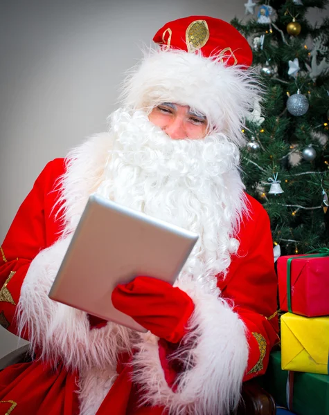Santa Claus con la tableta PC cerca del árbol de Navidad . — Foto de Stock