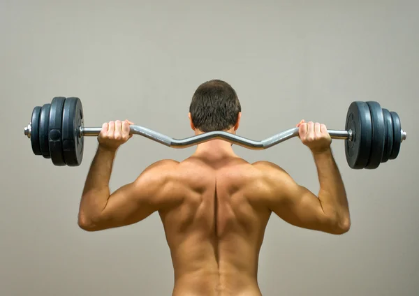 Kaslı adam barbell ile yapıyor. Arkadan Görünüm. — Stok fotoğraf