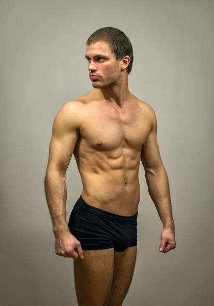 Mięśni model mężczyzna pozowanie na szarym tle. — Zdjęcie stockowe