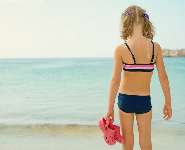 Little girl with flip flops standing on the beach. — Stock Photo, Image