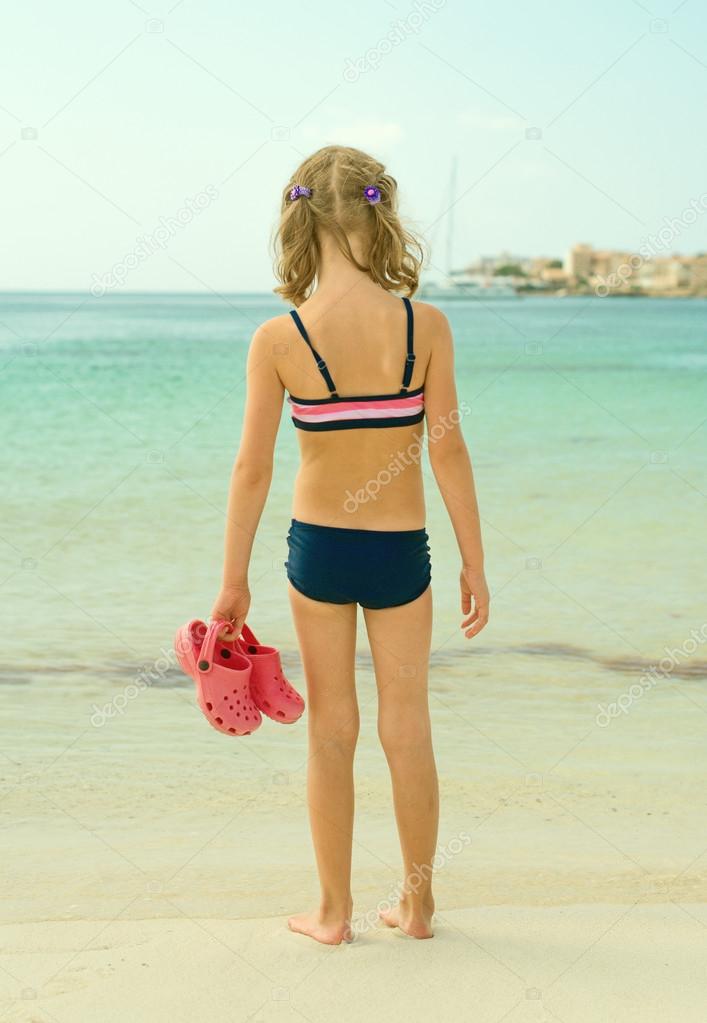 Little girl with flip flops standing on the beach.