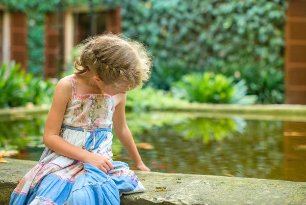 小女孩坐在有鱼的池塘. — 图库照片