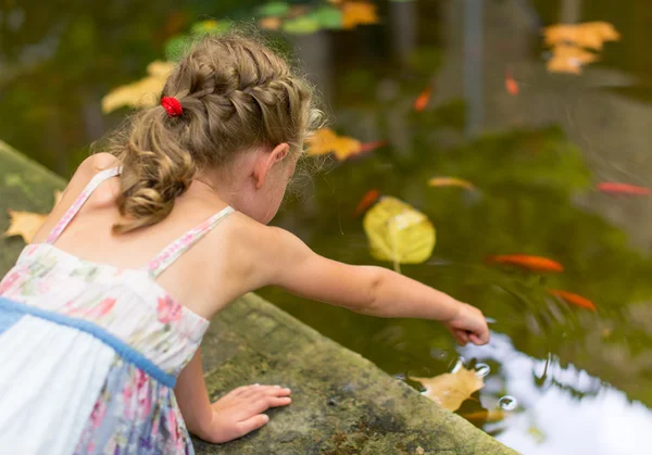 Kleines Mädchen am Teich mit Fischen. — Stockfoto