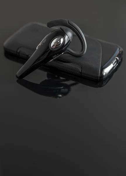 Primo piano del dispositivo bluetooth vivavoce vicino al telefono cellulare . — Foto Stock