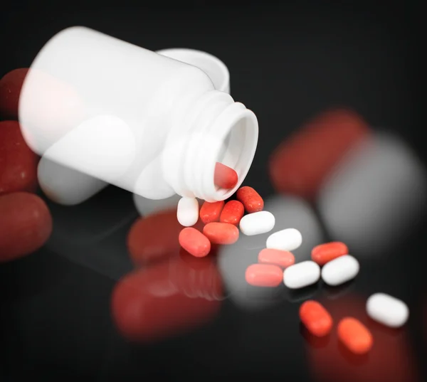 Red and white pills spilled from bottle. — Stock Photo, Image