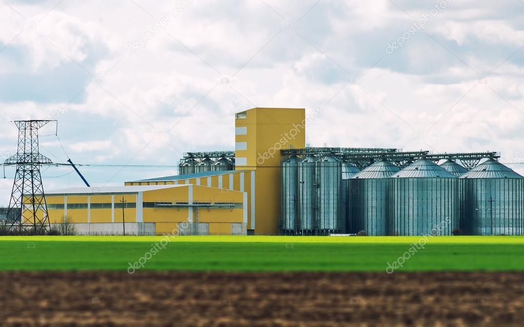 Factory and industrial silos near green field.