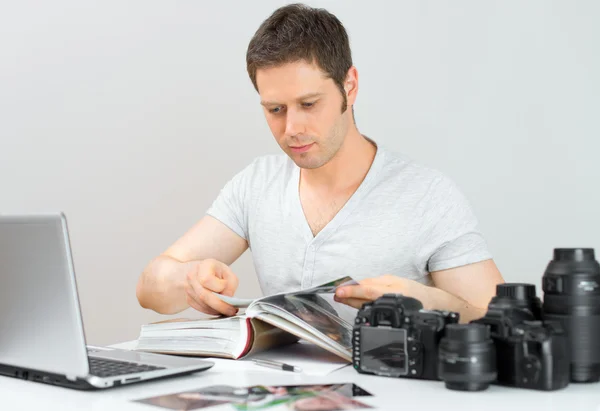 Hombre fotógrafo viendo álbum de fotos en su lugar de trabajo . — Foto de Stock