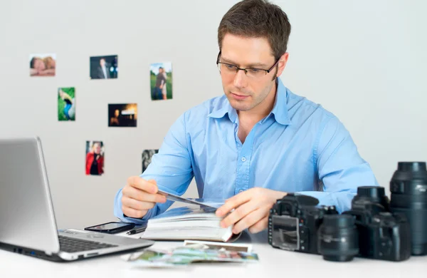 Hombre fotógrafo viendo álbum de fotos en su lugar de trabajo . — Foto de Stock