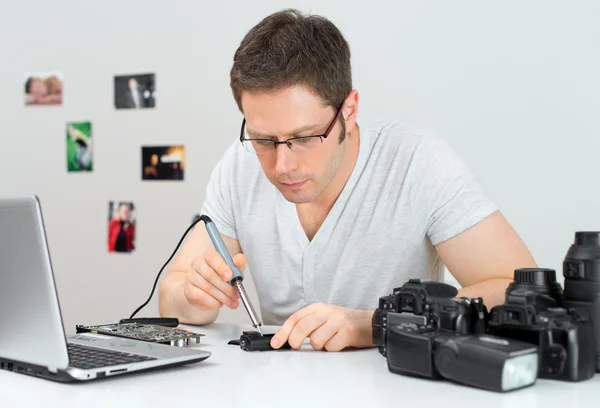 Fotógrafo soldando disparador flash inalámbrico en su lugar de trabajo . — Foto de Stock