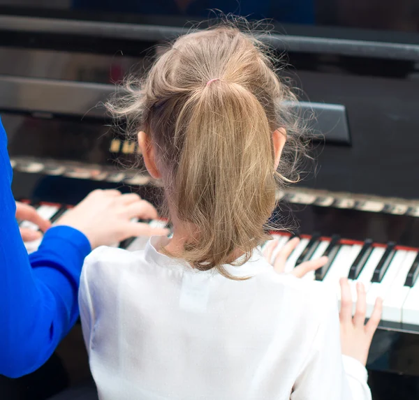 Mulher a ensinar a menina a tocar piano. Visão traseira . — Fotografia de Stock