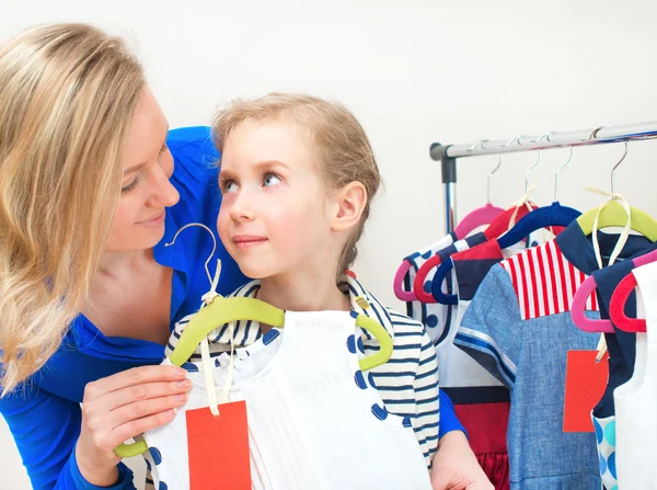 Klein meisje en haar moeder kiezen kleden in kledingwinkel. — Stockfoto