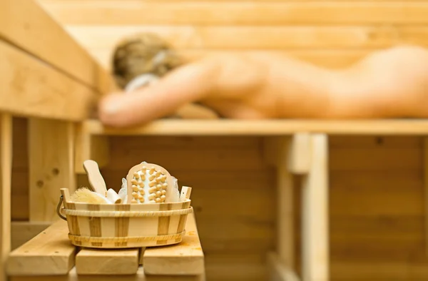 Wellnesszubehör in der Sauna. Frau im Hintergrund. — Stockfoto