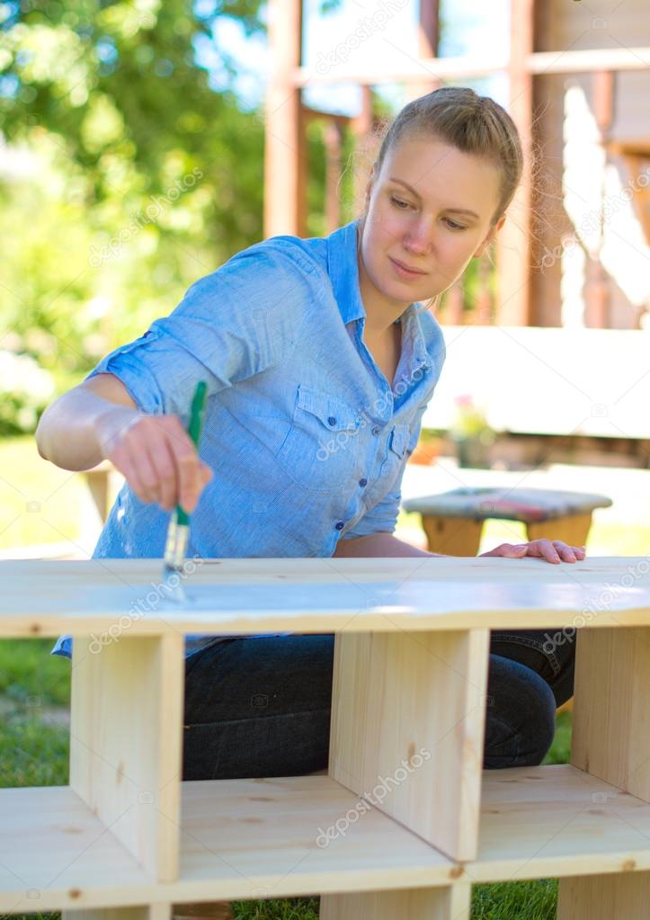 Woman with brush painting wooden furniture.