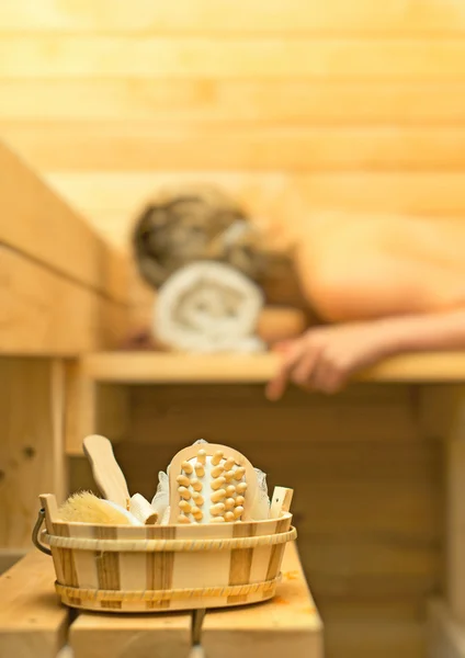 Wellnesszubehör in der Sauna. Frau im Hintergrund. — Stockfoto