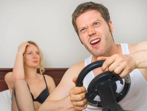 Video game addiction. Man playing video game with steering wheel, upset woman on background. — Stock Photo, Image