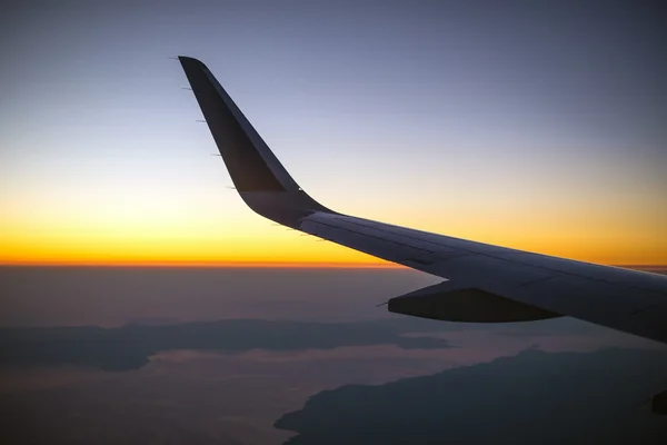 Vleugel van een vliegtuig bij zonsondergang, bekijken vanuit venster. — Stockfoto