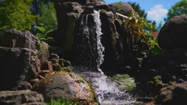 Küçük yapay şelale karanlık bahçe kayalarının üzerinden akıyor..