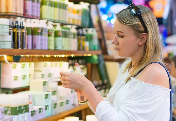 Młoda kobieta wybierając kosmetyk krem w salonie piękności. — Zdjęcie stockowe