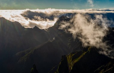 Bulutların üstünde rüzgar türbinleri olan dramatik dağ silueti..