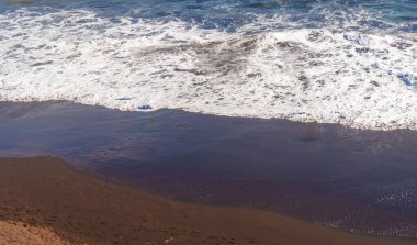 Okyanus dalgaları siyah volkanik kumu kaplıyor..