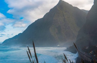 Kıyı kayalıkları ve bulutlu gökyüzünün altında okyanus dalgaları.