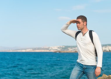 Sırt çantası konumu denize yakın olan erkek turist.