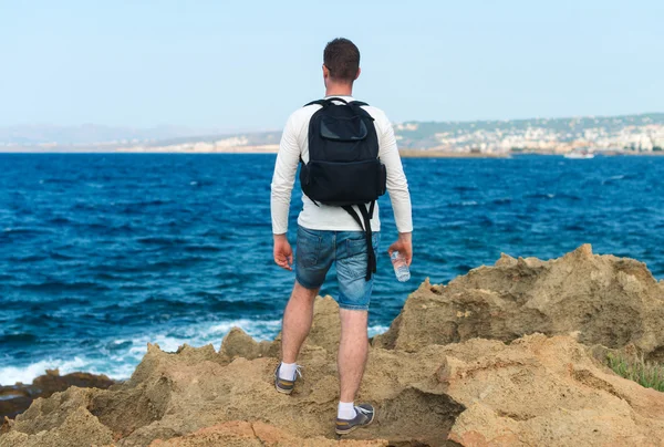 Ein männlicher Tourist mit Rucksack steht am Meer. Platz für Ihren Text. — Stockfoto