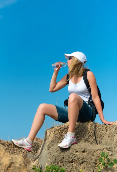 Female hiker rests on the rock and drinks water. — Stock Photo, Image