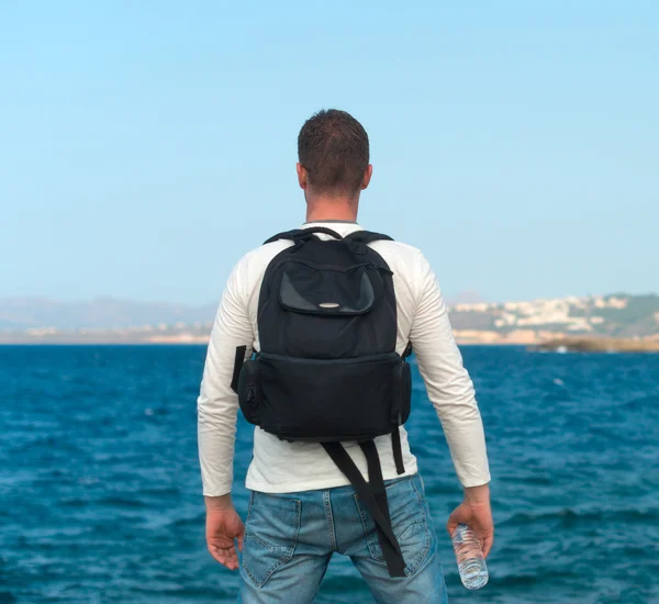 Ein männlicher Tourist mit Rucksack steht am Meer. Platz für Ihren Text. — Stockfoto