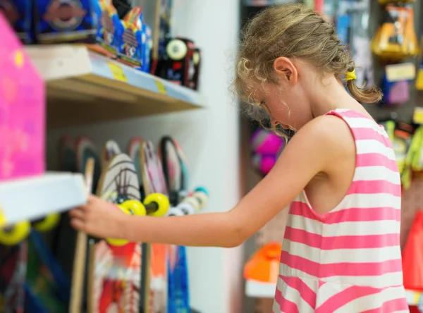 Kleines Mädchen wählt Skateboard im Supermarkt. — Stockfoto
