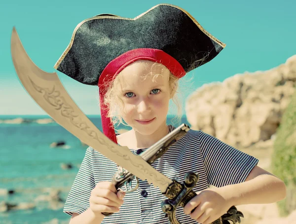 Kleines Mädchen im Piratenkostüm mit Schwert und alten Gewehren. — Stockfoto