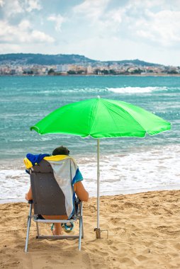 Adam rahatlatıcı plaj şemsiyesi altında.