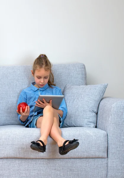 Petite fille assise sur le canapé et utilisant la tablette pc. Espace pour votre texte . — Photo