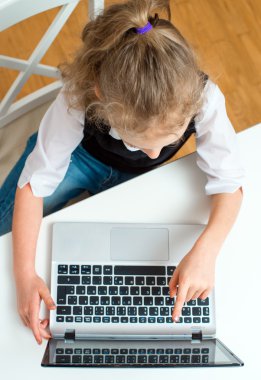 Dizüstü bilgisayar kullanan küçük kız ödevini evde yapıyor. Üstten Görünüm.