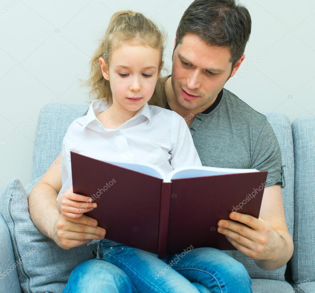 Father reading book with daughter at home.