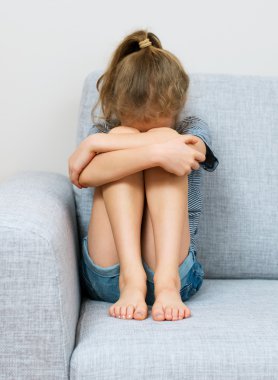 Üzgün küçük kız kanepede ağlıyor.