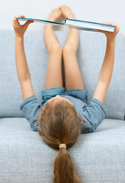 Lilla flickan läsa bok i soffan. — Stockfoto