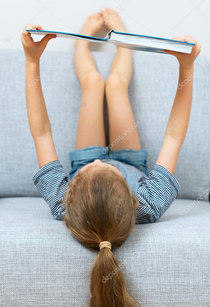 Little girl reading book on the sofa.