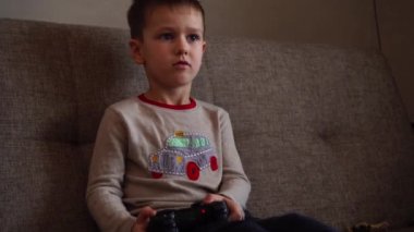 Kanepede oturmuş video oyunu oynayan küçük çocuk.