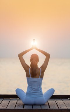 Gün batımında plajda yoga yapan genç bir kadın.