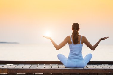 Gün batımında plajda yoga yapan genç bir kadın.