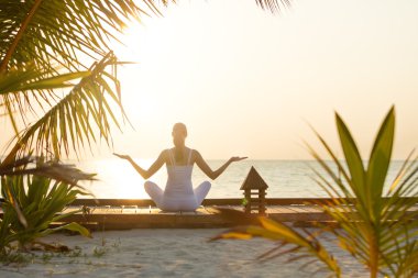 Gün batımında plajda yoga yapan genç bir kadın.
