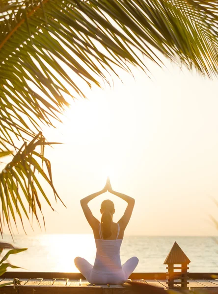 Jovem praticando ioga na praia ao pôr do sol — Fotografia de Stock