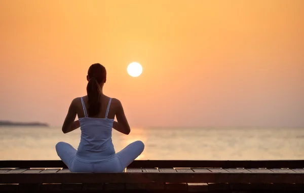 Gün batımında plajda yoga yapan genç bir kadın. — Stok fotoğraf